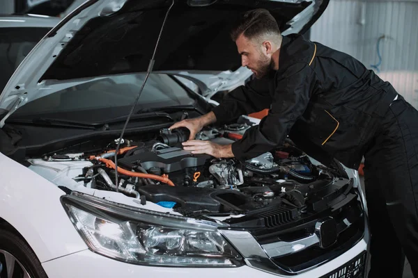 Chico mecánico bien parecido trabajando en el motor del coche resolver el problema delante de la cámara que trabaja muy concentrado — Foto de Stock