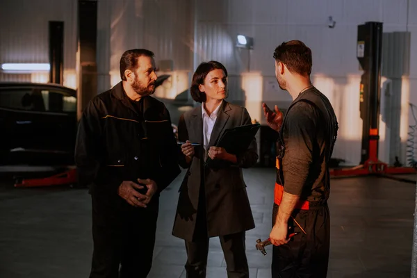 Remek csapat egy autószerelő központ irodavezetőjével és két szerelővel beszélgetnek a garázs közepén. Elemeznek valamit. — Stock Fotó