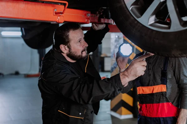 Een grappige werknemer analyseert de auto van onderen, zeer geconcentreerd — Stockfoto