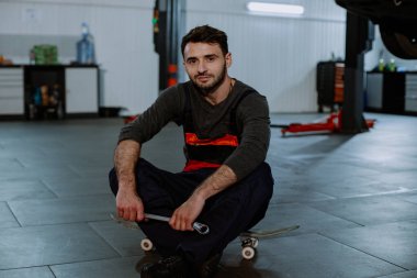 Genç bir tamirci, bir araba servisinde kaykayın üzerinde oturuyor.