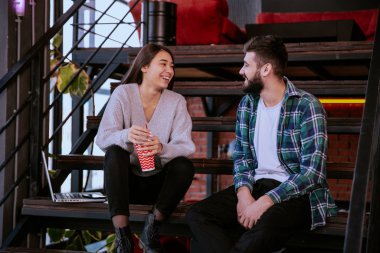 Modern çalışma stüdyosunda yakışıklı bir erkek ve güzel bir bayan merdivenlerde oturup güzel bir sohbet ediyor.