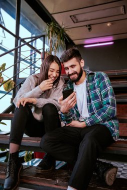 Modern çalışma odasında güzel bir erkek ve güzel bir bayan gülümsüyor merdivenlerde oturup komik bir video izliyorlar.