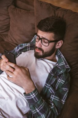 Evde kanepede yatarken cep telefonu kullanan adam. Yaşam tarzı konsepti, teknoloji