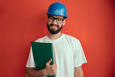 Koruyucu miğfer ve beyaz gömlekli başarılı genç mühendis elinde belge ve kalemle tecrit altında.