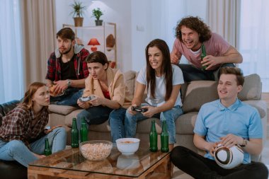 Büyük geniş oturma odasında büyük bir grup arkadaş Tv önünde bir maç izlerken çok heyecanlı ve kanepede oturan konsantre