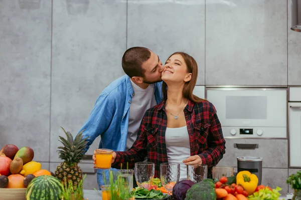 Casal jovem romântico atraente olhando fazendo juntos o café da manhã saudável juntos de frutas e legumes beijando uns aos outros — Fotografia de Stock