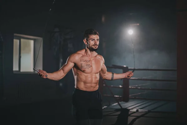 Detalles de un atleta usando una cuerda de salto cruzada para hacer sus ejercicios de entrenamiento duro en una clase de gimnasia oscura — Foto de Stock