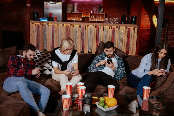 Група студентів має соціальний проект в сучасній бібліотеці коледжу вони сидять на дивані всі грають по телефону — стокове фото