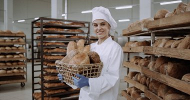 Beyaz üniformalı güzel bayan fırıncı taze ekmek ile bir sepet tutan ve kamera önünde sevimli gülümseyen