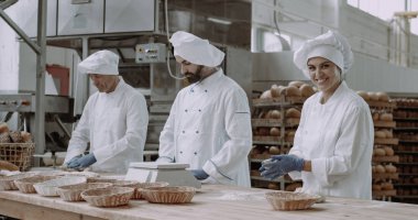 Çok karizmatik bir fırıncı kadın büyük bir gülümseme ve iş arkadaşları ekmek pişirmek için hamur oluşturuyorlar, ekmek yapma süreci, gıda endüstrisi.