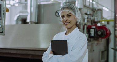 Büyük bir imalat sanayi fabrikasında elektronik tablet tutarken kamera düz görünümlü ve büyük gülümseyen olgun bir kadın çekici mühendis Closeup portre