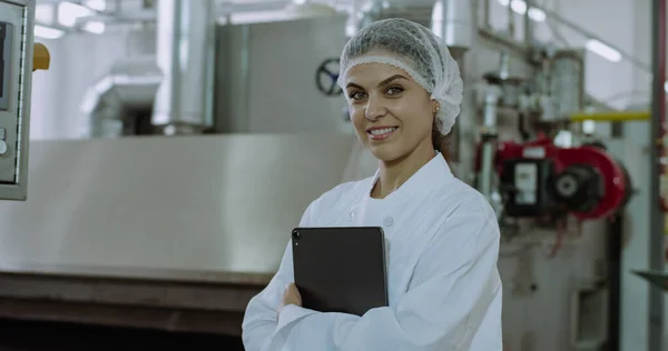 Primo piano ritratto di una donna matura attraente ingegnere guardando dritto della fotocamera e sorridente grande mentre tiene in mano un tablet elettronico in una grande fabbrica industriale — Foto Stock