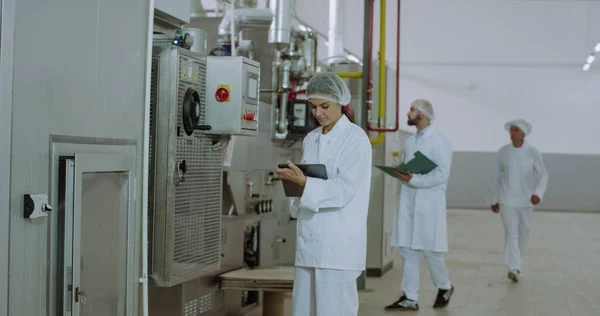 Al mattino due bellissimi ingegneri dell'industria manifatturiera controllano la macchina industriale e prendono appunti sul tablet elettronico — Foto Stock