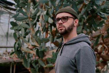 Santralin yanında duruyor. Serada bitkinin yanında duran açık tenli ciddi bir erkek model.