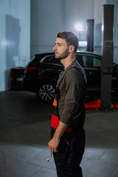 Mechanische man in een uniform serieus in de voorkant van de camera in een moderne auto service center — Stockfoto