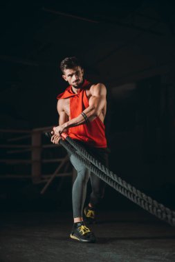 Çapraz fitness sınıfında idman yaparken kaslı vücutlu yakışıklı, halatla egzersiz yapan biri sert ve konsantre bir yüz yapar.