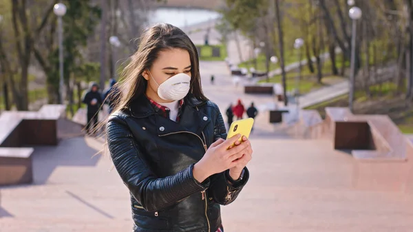 Mitten im Park hält eine Dame mit Schutzmaske ihr Handy in der Hand — Stockfoto
