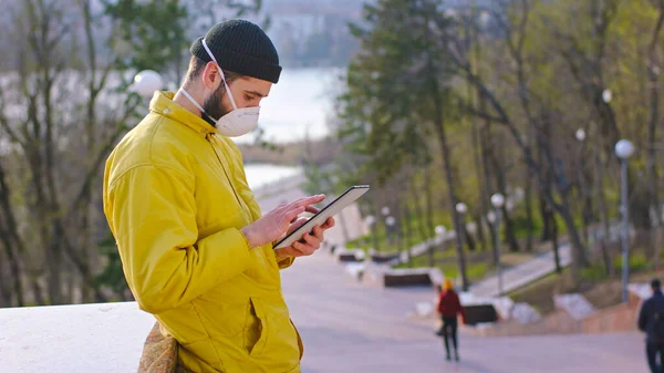 Mitten im Park steht ein Mann mit Schutzmaske auf seinem Tablet. — Stockfoto