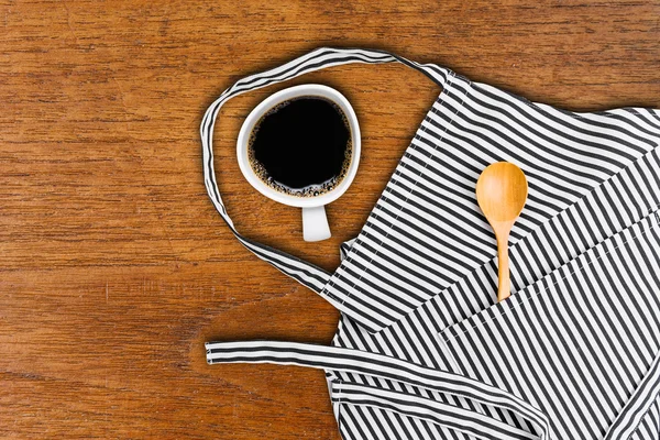 Cup of coffee and kitchen utensils in pocket of apron