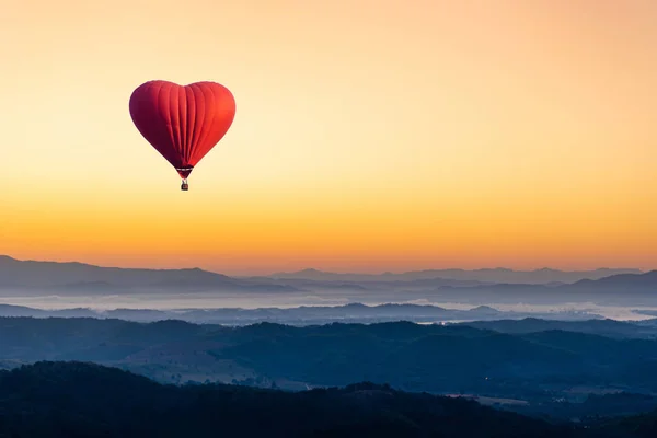 Balão de ar quente vermelho na forma de um coração voando sobre o moun — Fotografia de Stock