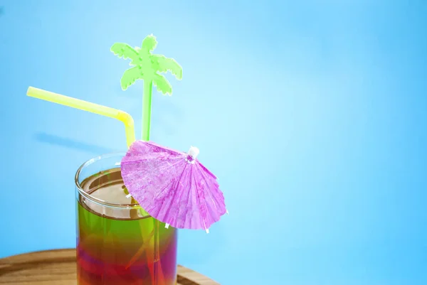 Colored layered cocktail with a straw and decor on a blue background