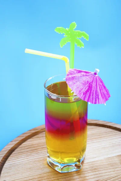 Colored layered cocktail with a straw and decor on a blue background
