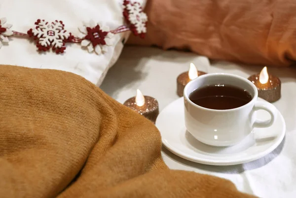 White cup of tea. Home textiles. Brown plaid, beige aroma, New Year\'s decor, candles. Tinted. Space. Life stile.