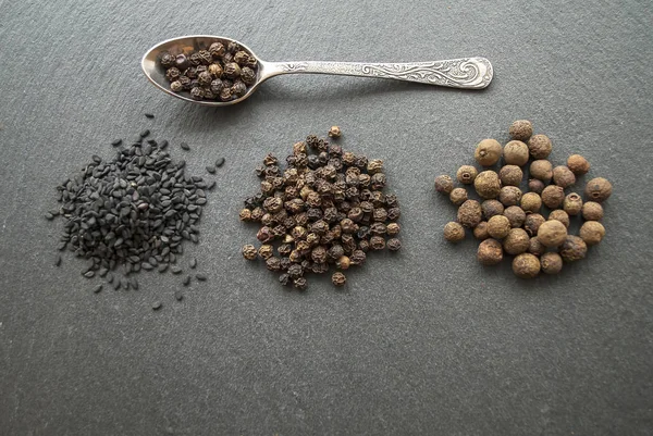 Black sesame seeds, peas, allspice. Spices on a dark background. a rock