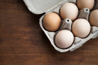 Tahta bir tahtanın üzerinde, karton bir tepside parlak yumurtalar. Boşluğu kopyala