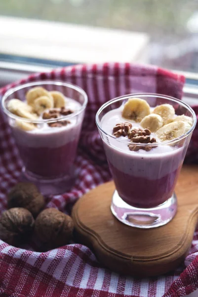 Two glasses of yogurt with banana and nuts on a textile
