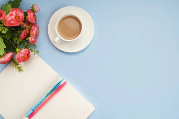 White cup of coffee and notebook for notes on a blue background. Place for text. Flat lay