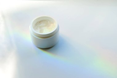 Beyaz arka planda beyaz bir krema şişesi. Mesaj için yer. Gökkuşağı taşkınlığı