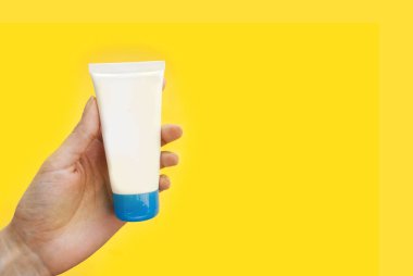 Sarı arkaplandaki krema şişesiyle ilgilenmek. Metin için yer.