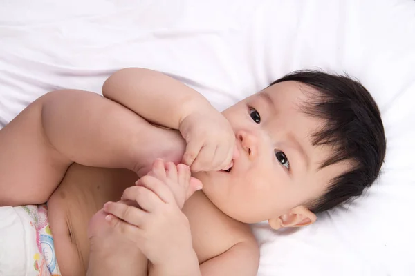 Retrato de bonito pouco ásia menino 6 meses idade colocar seu dedo do pé na boca no o branco cama — Fotografia de Stock