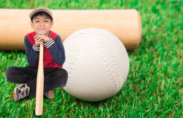 Liten pojke sitter med basebollträ på gräset — Stockfoto