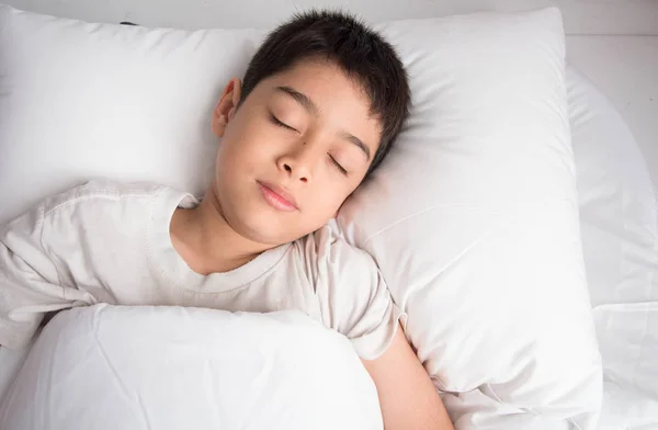Маленький хлопчик спить у ліжку з білою кришкою ковдри — стокове фото