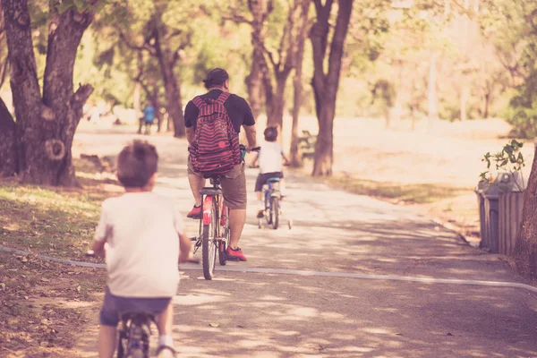 Padre y hermanito montan juntos en bicicleta en el parque — Foto de Stock