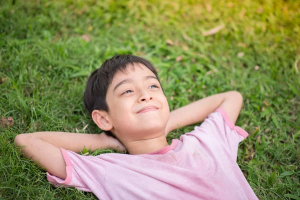 Menino deitado na grama no parque com o rosto sorridente como sonhando — Fotografia de Stock