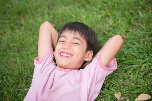 Маленький мальчик лежал на траве в парке с улыбающимся лицом, как во сне — стоковое фото