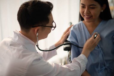 Asyalı doktor ve hasta hastanede sağlık sigortası hastalığını konuşuyor ve kontrol ediyor.