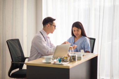 Asyalı doktor ve hasta hastanede sağlık sigortası hastalığını konuşuyor ve kontrol ediyor.