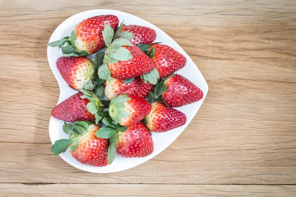 Fragole in piatto a forma di cuore sul pavimento in legno — Foto Stock