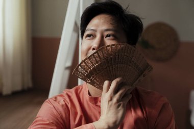 Asyalı gey gülümsemesi odasında oturmuş dışarıyı arıyor. Kendisi olduğu için mutlu..