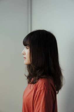 Beyaz duvarın önünde tek başına duran Taylandlı kızın sol tarafı..