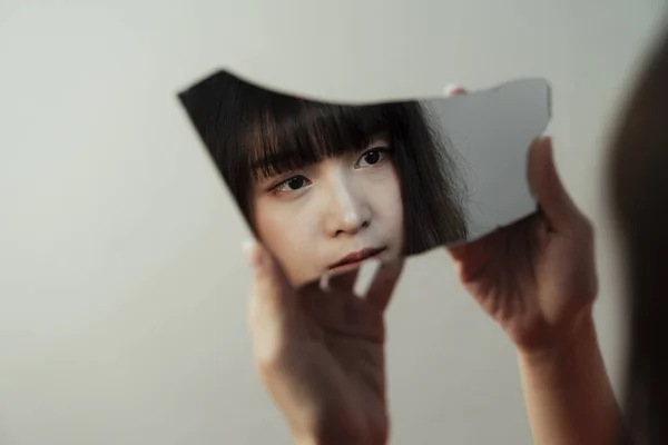 Thai girl hold the broken mirror in her hands but her reflection shows that her eye sight is empty.