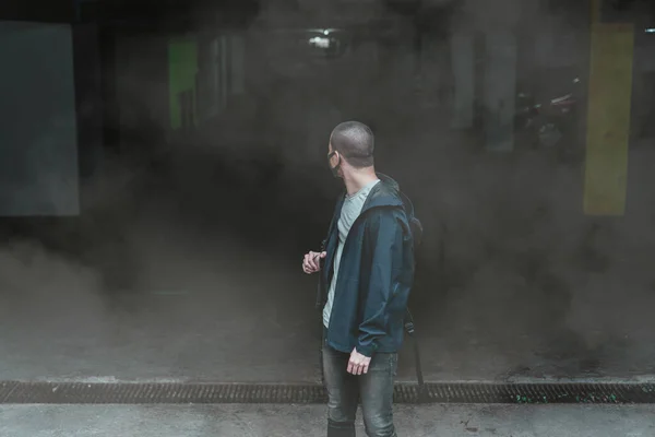 man wearing a real anti-pollution, anti-smog and viruses face mask; dense smog in air and holding big bags, He look at the back while standing at the parking lot