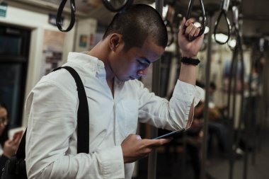 İşini bitirdikten sonra eve dönmek için trenle giderken telefonunu kontrol eden bir adam..