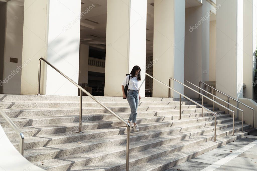 College girl walking down the stair after she finish her reading at the library.