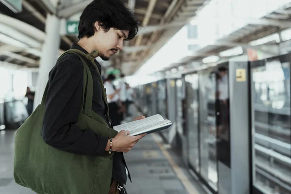 Guy reading a book on skytrain platform.