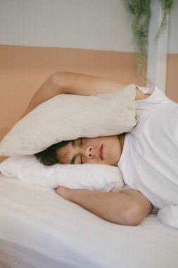 Yataktaki adam rahatsız olduğu için kulaklarını yastıkla kapatıyor..